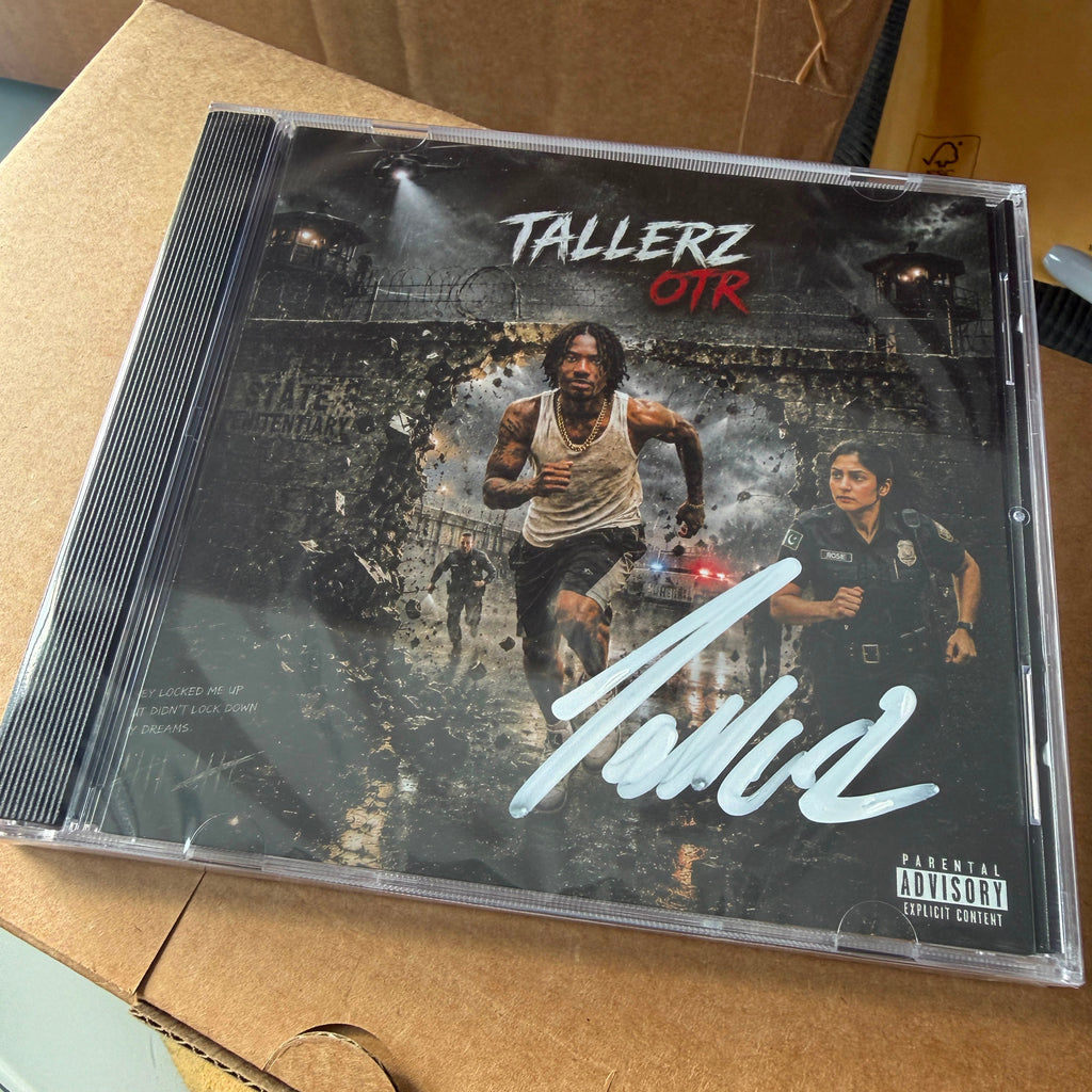 A CD case for the album 'Tallerz OTR' by the artist Tola, resting on a brown cardboard box. The album cover features a dark, gritty scene with two men, one in a tank top and one in a police uniform, with a large white signature across the front and a Parental Advisory label in the bottom right corner.